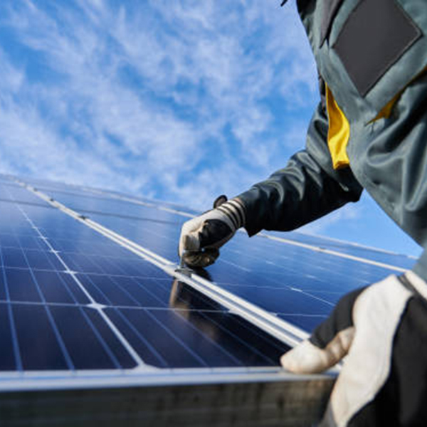 Close-up van een man-technicus in werkhandschoenen die een zelfstandig fotovoltaïsch zonnepaneelsysteem installeert onder een prachtige blauwe hemel met wolken.Concept van alternatieve energie en duurzame energiebronnen.